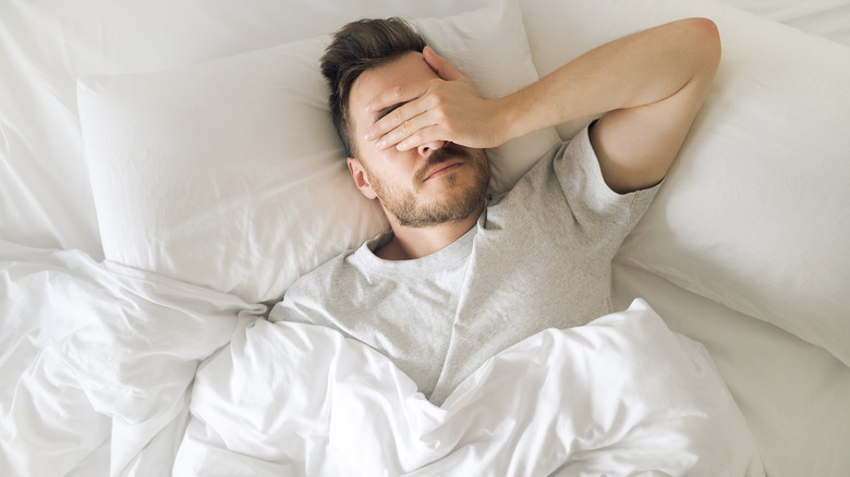 tired and hungover man lying in bed 