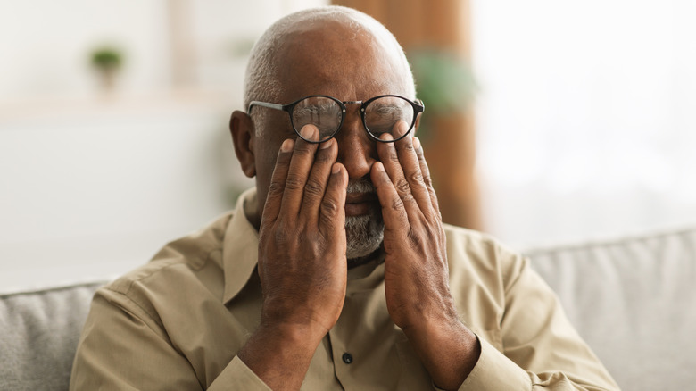 an older man rubs dry eyes