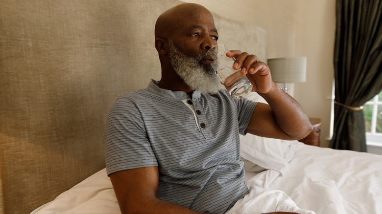 Man drinking glass of water in bed