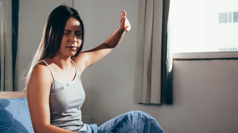 woman using her hand to block sunlight from her room 