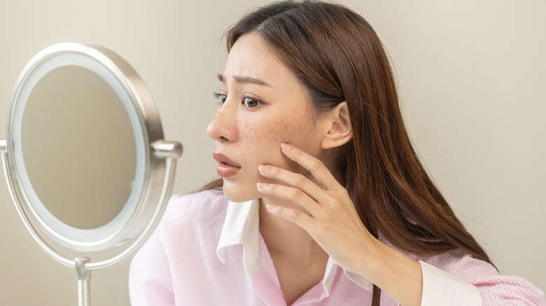 woman looking at skin in mirror