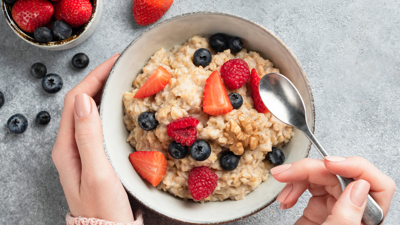 Hands holding bowl of oatmeal porridge with berries