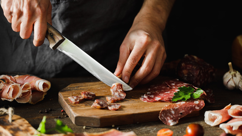 woman cutting pieces of salami on a cutting board