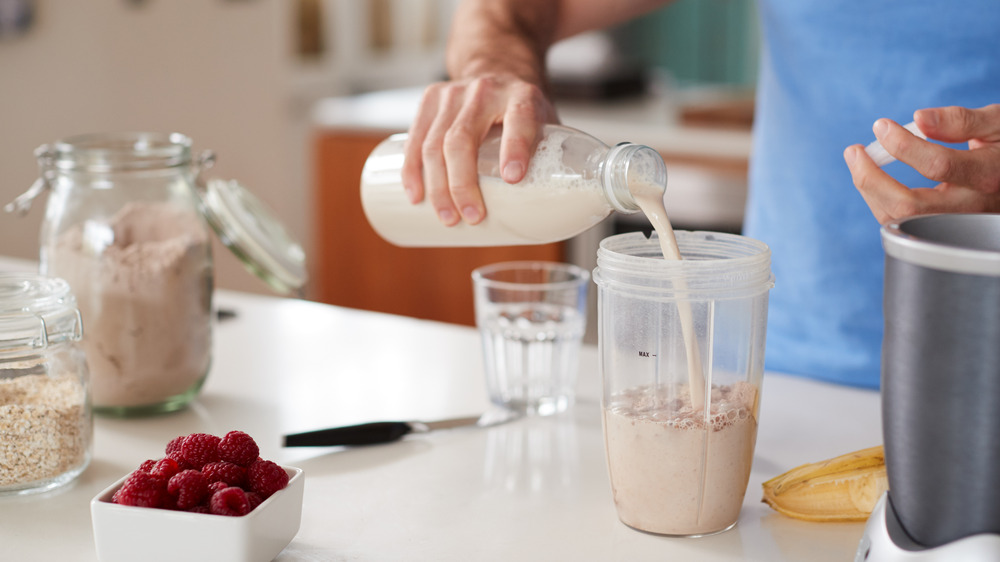 A man makes a protein shake in his kitchen.