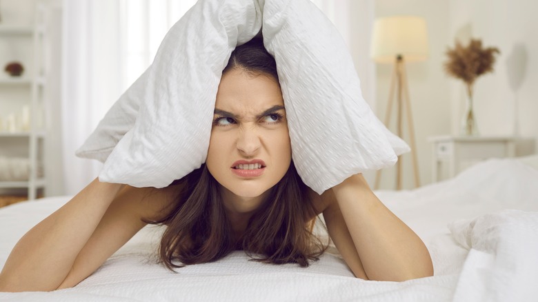 woman in her bed looking grumpy with a pillow over her head