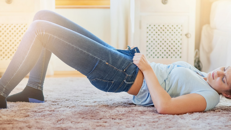A woman in discomfort lying down trying to pull on tight pants