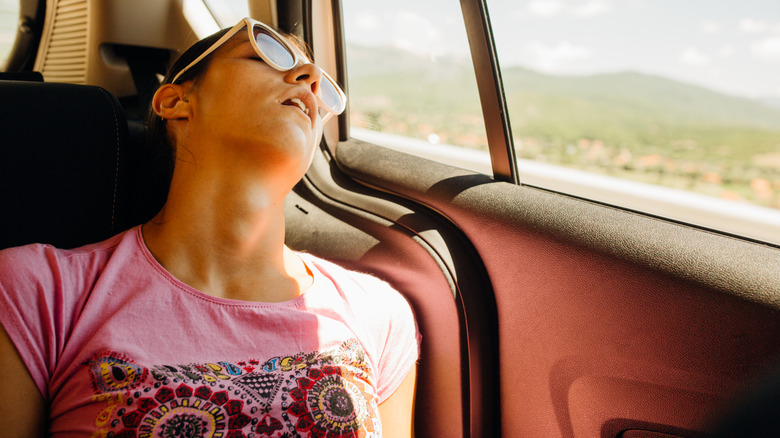 Woman in sunglasses asleep against car window on road trip