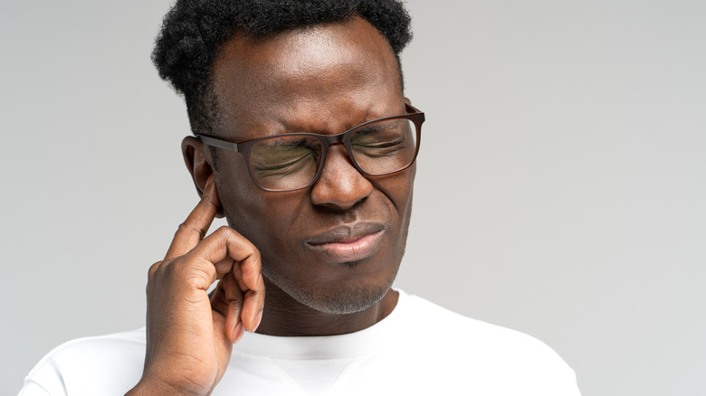 man wincing while holding his ear