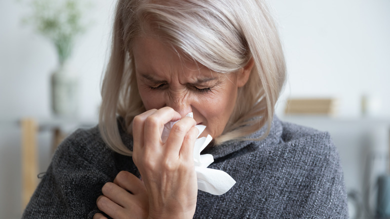 Older woman sneezing and covering her mouth with a tissue