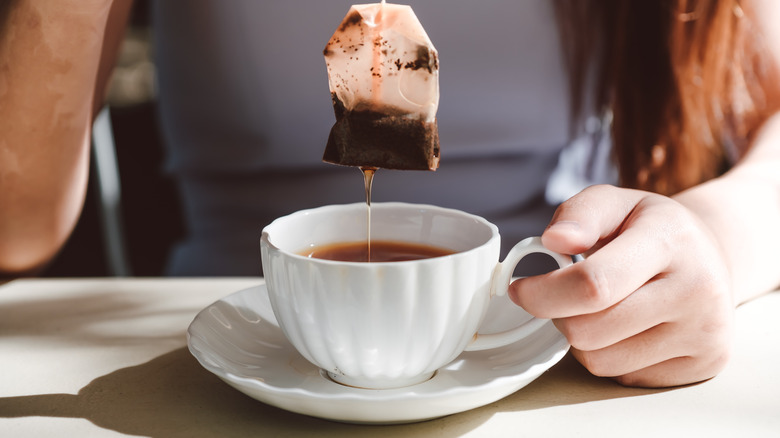 women pulling out a tea bag from her cup of tea