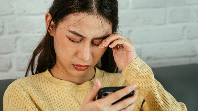 Woman holding smartphone and rubbing eyes