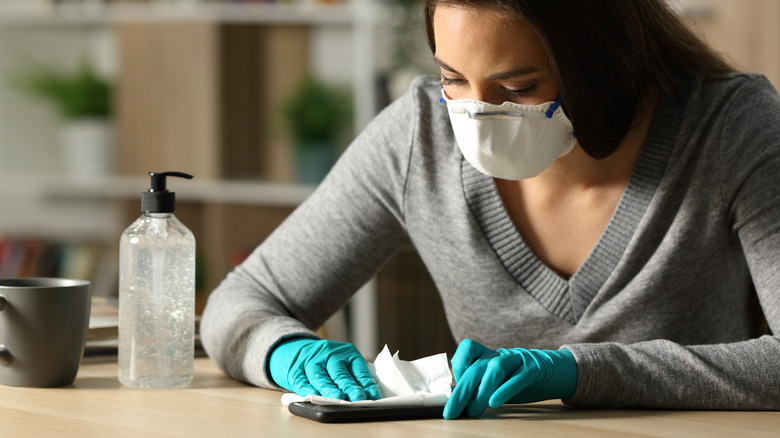 masked woman cleaning germs off cell phone