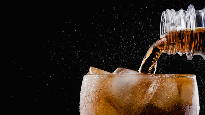 fizzy diet soda being poured into a glass with ice 