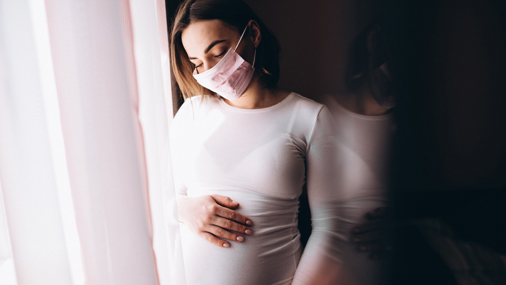 pregnant woman looking out the window wearing a face mask 