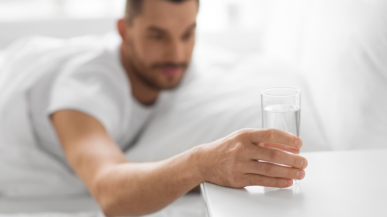 Man reaches for water from bed