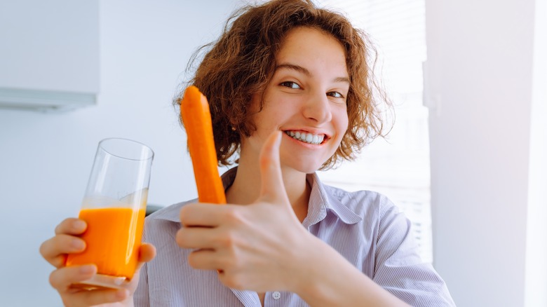 Woman holding a carrot and a glass of carrot juice