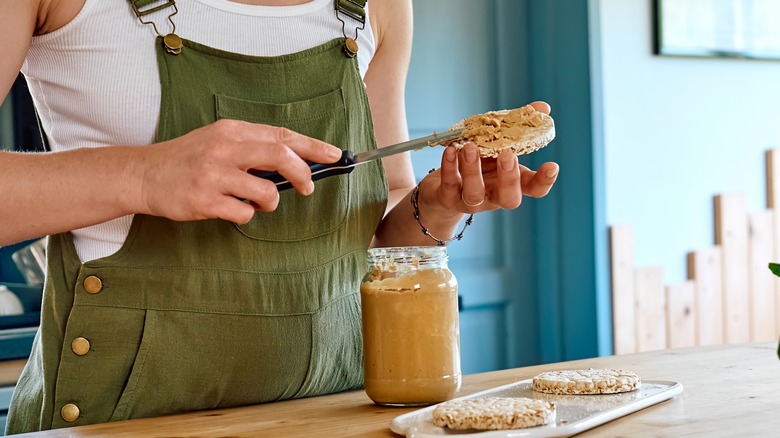 Hands spreading peanut butter on rice cake