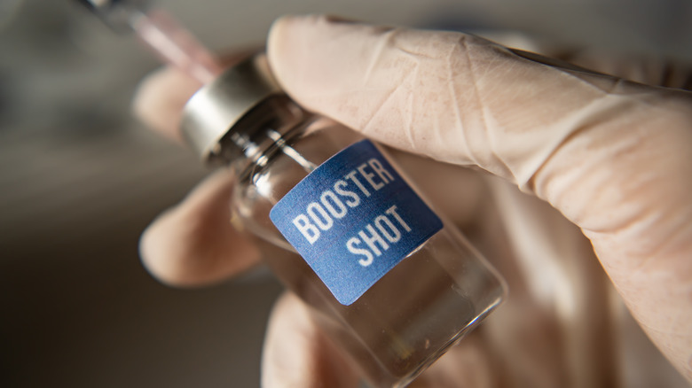 Gloved hand holding booster shot vial of COVID-19 vaccine