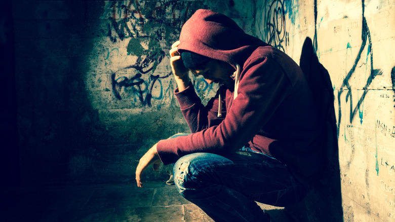 man wearing hood squatting in a dark alley