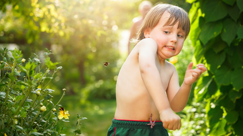 A shirtless young boy avoiding a bee