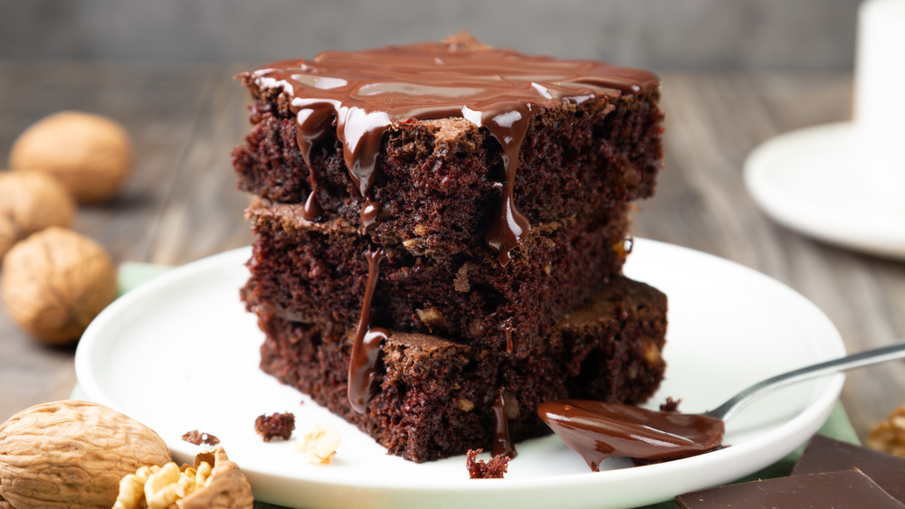 A three layered piece of chocolate cake topped with chocolate frosting 