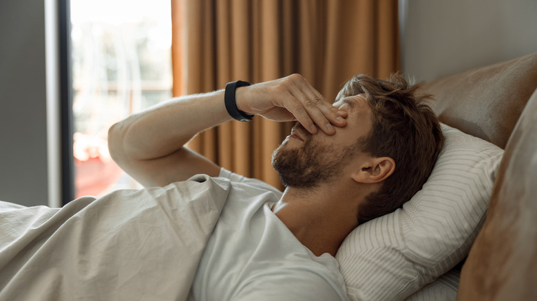 man lying in bed rubbing eyes