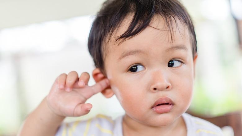 worried toddler touching ear