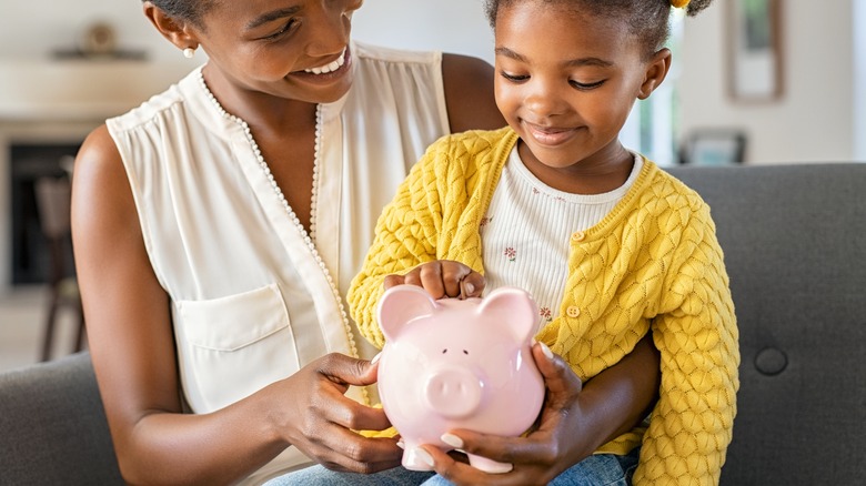 a mom and daughter putting money in a piggy bank