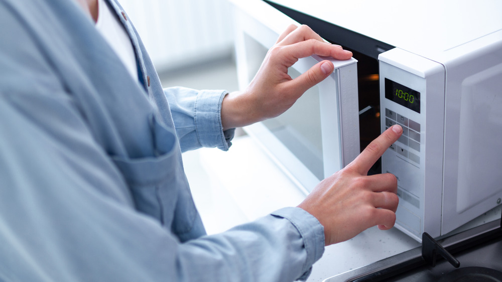 Person pressing numbers on microwave while holding door