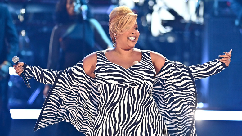 Lizzo performing onstage during a concert while wearing a flowing black and white dress