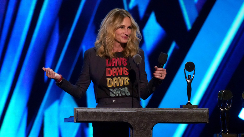 Julia Roberts lifts her arms while speaking on stage at an event