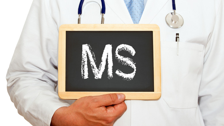 A doctor in white lab coat holding up a chalkboard with the letters MS written on it