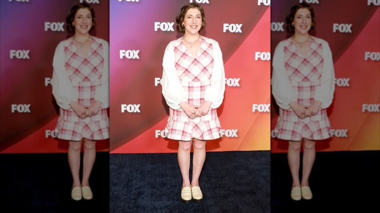 Mayim Bialik posing at a celebrity event in a pink and white dress