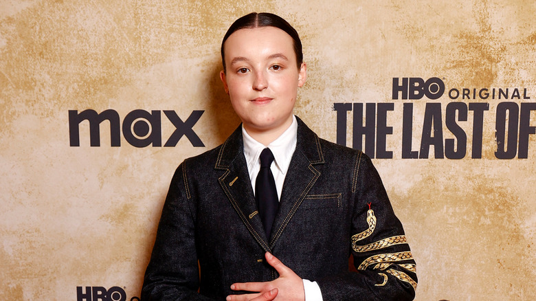 Bella Ramsey in a denim suit with their hair slicked back in front of a tan background for the last of us.