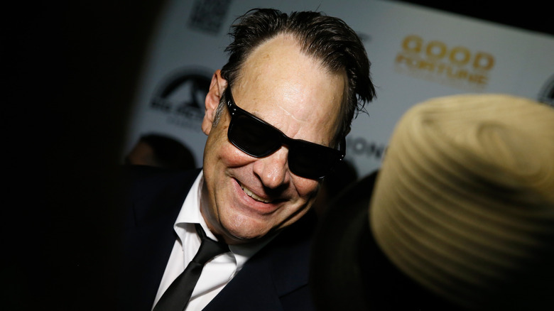 Dan Aykroyd in sunglasses, leaning into a reporter's space.