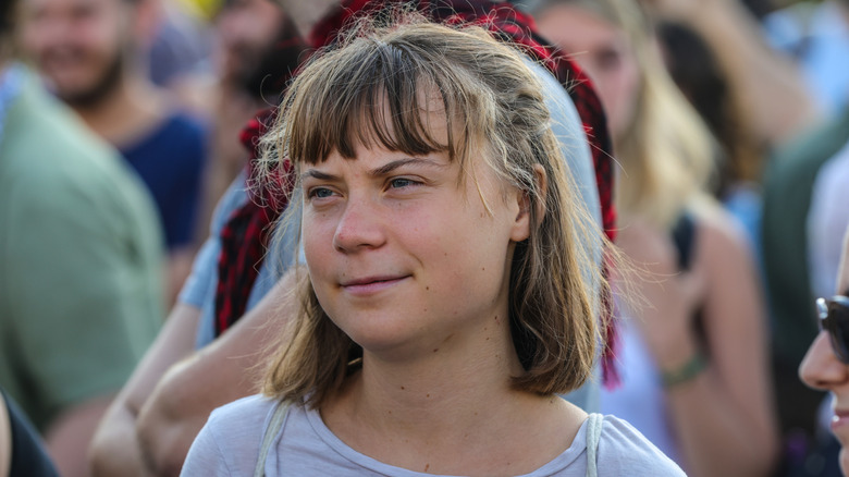 Among a crowd of people, blurred, Greta Thunberg in a gray shirt and frizzy hair.