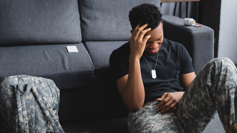 Soldier sitting in front of a couch with his hand on his head