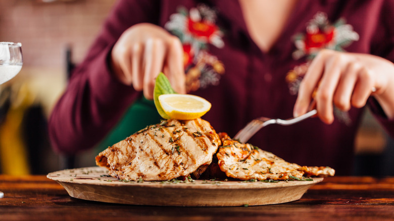 woman cutting chicken on plate at table