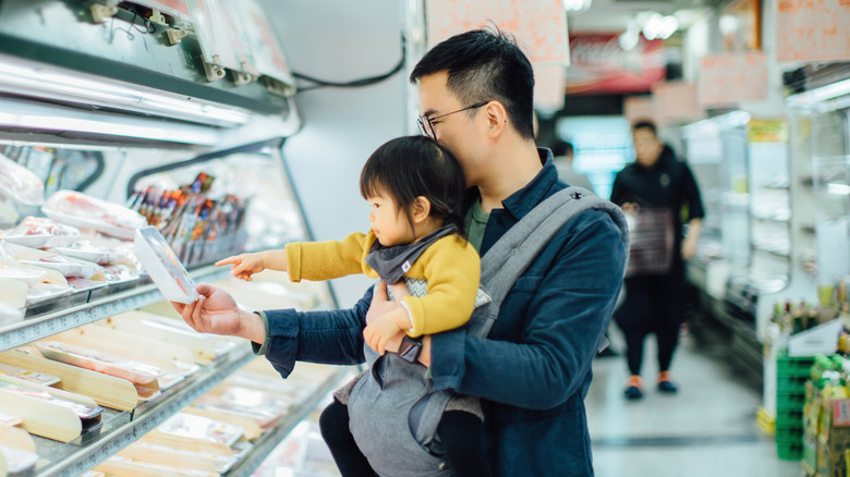 father with daughter choosing chicken parts at the store