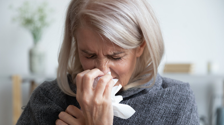 Older woman sneezing into tissue
