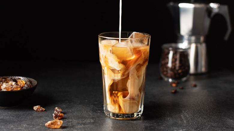 Milk pouring into glass with iced coffee