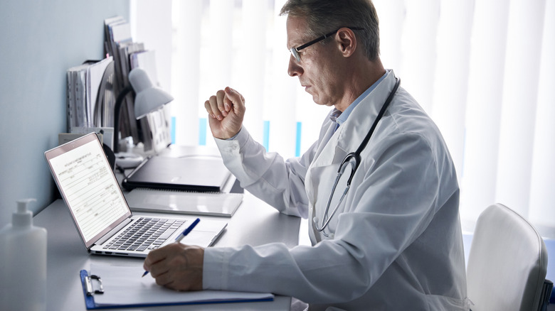 A male doctor reading on a laptop