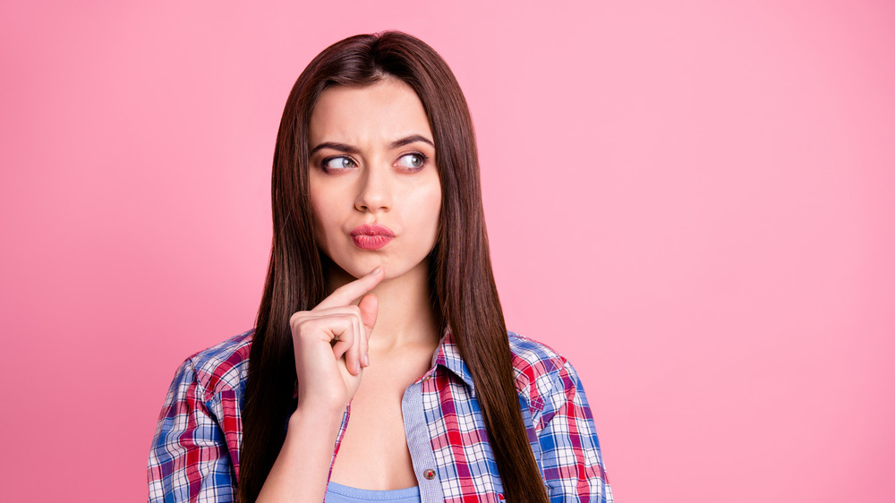 Young woman trying to make up her mind, all pink background 