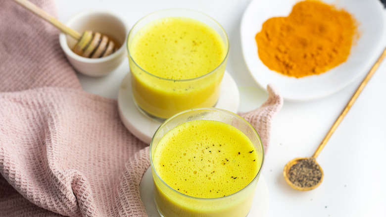 Two glasses of turmeric latte next to a napkin, honey, turmeric, and black pepper