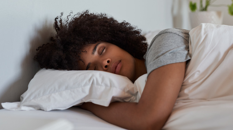 A young woman asleep in a bed with white sheets