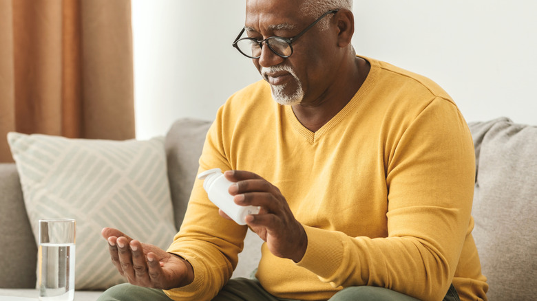 mature man taking vitamin pill with water while on sofa