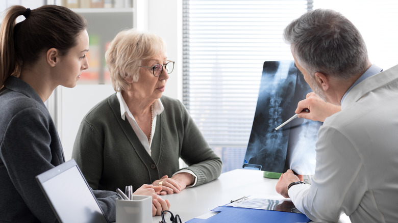 Two patients sitting in doctors office while doctor points to a spinal x-ray 