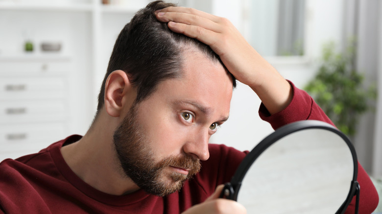 A man looking in the mirror at his receding hairline