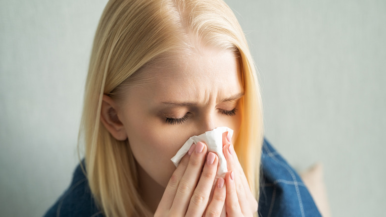 sick woman using tissue on her nose