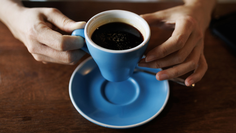 Person holding a ceramic cup of coffee while sitting at a table